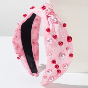 Vue détaillée du serre-tête noué rose avec imprimés cœurs et perles rouges décoratives
