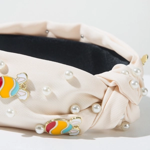 Detail eines beigen Knotenstirnbandes mit Kunstperlen und bunten Emaille-Anhängern