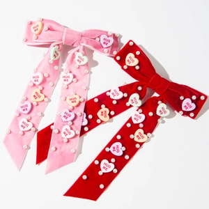Detail van een fluwelen haarclip met parels en HUG ME hartvormige bedeltjes in roze en rood