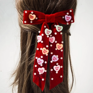 Detailopname van een rode fluwelen haarstrik met parels en Hug Me hartjesbedeltjes