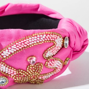 Gros plan des motifs de perles en cœur et strass roses sur un serre-tête noué magenta