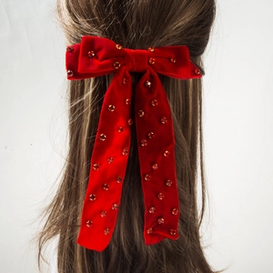Détail d'une barrette à cheveux nœud en velours rouge avec strass sur cheveux bouclés