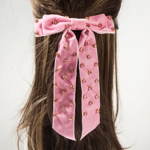 Détail d'une pince à cheveux avec nœud en velours rose orné de strass et de longs rubans