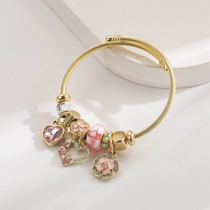 Detail of golden charm bracelet featuring pink heart crystals and floral enamel pendants