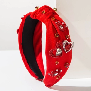 Dettaglio di fascia per capelli rossa annodata con decorazioni di cuori e corona di strass