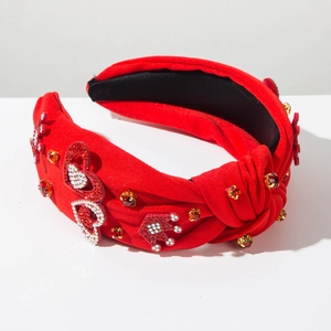 Dettaglio di cerchietto rosso annodato con strass lucidi, motivi a cuore e corona