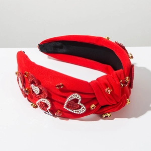 Dettaglio fascia rossa annodata con motivi a cuore in strass e borchie in rubino dorate