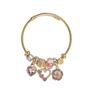 Detail of a golden spiral bracelet with pink heart crystals and enamel flower charms