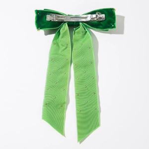 Détail d'une pince à cheveux nœud en velours vert avec rubans organza et strass argentés