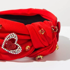 Dettaglio di cerchietto rosso annodato con strass a cuore e gemme rosse brillanti