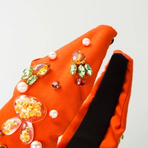 Detail of orange fabric headband with colorful rhinestones and white pearls