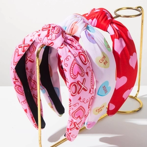 Close-up of three Valentine's knot headbands with XOXO and heart prints on a gold stand