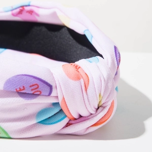Detail of a pink knotted headband with colorful heart candy prints and Be Mine text