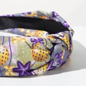 Detalle de diadema anudada con lazo morado y estrellas doradas sobre tela suave