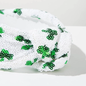 Detailed close-up of a knotted headband featuring green sequins clover on white fabric