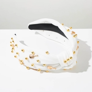 Détail d'un bandeau blanc noué orné de rivets dorés et de breloques en forme de raquette
