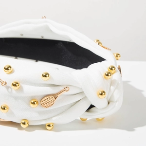 Détail d'un serre-tête blanc noué avec des boules en métal doré et un pendentif de raquette