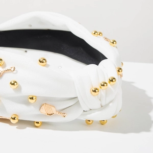 Détail du serre-tête en tissu blanc avec perles dorées et breloque de raquette