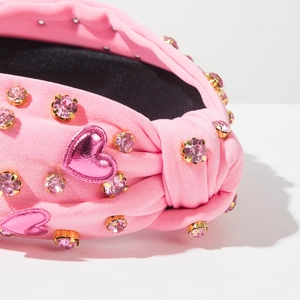 Detailansicht eines rosa Strickstirnbands mit Kristall-Strass und Herz-Patches