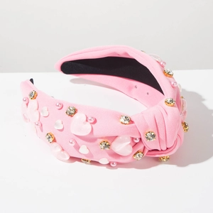 Détail d'un serre-tête rose noué orné de pierres en cœur, de perles et de cristaux brillants