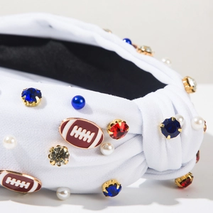 Detail of white knotted headband with rugby football charms and colorful rhinestones
