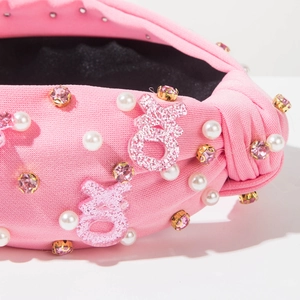 Détail du bandeau rose noué avec lettres XOXO scintillantes et perles élégantes