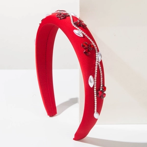 Détail d'un serre-tête en velours rouge avec cristaux floraux et perles sur support blanc