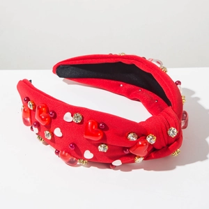 Détail d'un serre-tête rouge avec nœud, cœurs, perles et strass brillants
