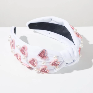 Detail of white knotted headband with pink rhinestone hearts and pearls on fabric