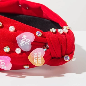 Macro detail of red knotted headband featuring pearls and hearts with BE MINE text