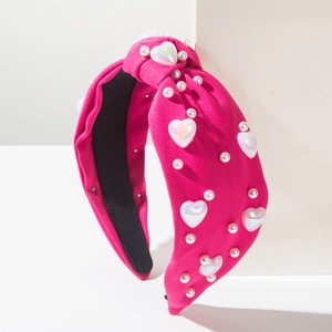 Détail d'un serre-tête noué rose fuchsia avec perles blanches et ornements en cœur