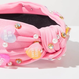 Detail of pink knotted headband featuring faux pearls, colorful rhinestones, and heart charms