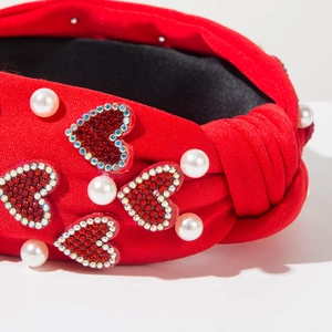 Close-up of red knotted headband with rhinestone hearts and white faux pearls decor