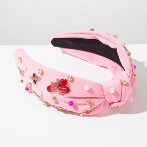 Détail du serre-tête rose noué avec breloque cœur LOVE, perles et strass scintillants