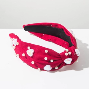 Détail d'un serre-tête rouge noué avec petites perles et breloques en forme de cœur nacré