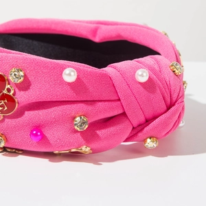 Détails du serre-tête fuchsia noué avec perles, strass et pendentif cœur en vue macro
