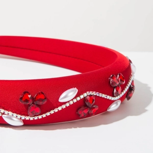 Détail d'un serre-tête en velours rouge avec cristaux en cœur et perles blanches