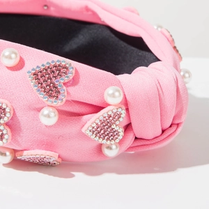 Detail of pink knitted knotted headband with faux pearls and sparkling rhinestone hearts