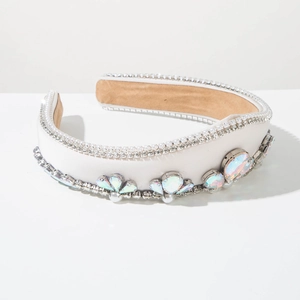 Dettaglio di cerchietto in raso bianco con strass aurora e perle su sfondo grigio chiaro