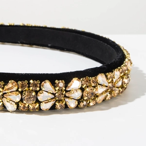 Close-up of champagne and clear rhinestones hand-set on a black velvet headband surface
