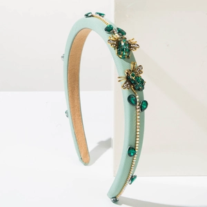Detailed macro view of mint green fabric headband with golden bees and emerald rhinestones