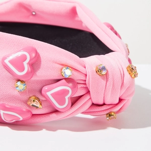 Detailweergave van de roze gebreide hoofdband met knoop, kristallen en hartjesversiering