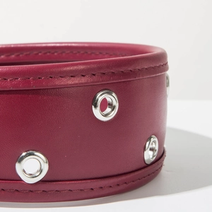 Gros plan sur un serre-tête en cuir rouge foncé avec œillets métalliques et coutures fines