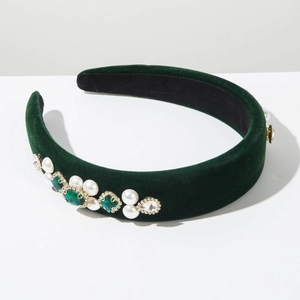 Close-up of green velvet headband featuring emerald gems, white pearls and gold accents