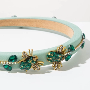 Detail of mint green satin headband with emerald gemstones and golden bee crystal accents