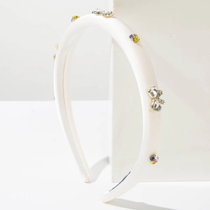 Détail d'un serre-tête en satin blanc orné de strass colorés sur un socle géométrique