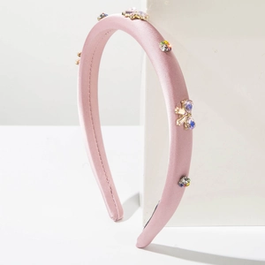 Détail du serre-tête en satin rose avec strass colorés et nœud en cristal sur pierre