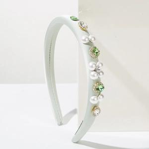 Detailed close-up of light green satin headband with pearls and green rhinestones