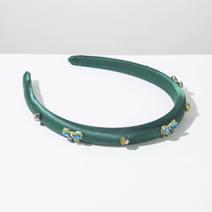 Détail du serre-tête en satin vert foncé avec papillon en cristal et strass colorés