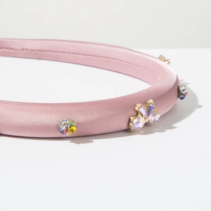 Détail macro du serre-tête en satin rose avec strass colorés et papillon en cristal